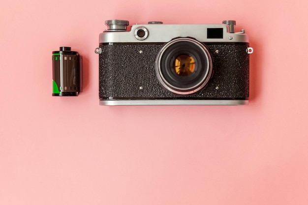 Vintage-Film-Fotokamera-Objektiv und Filmrolle auf rosa pastellfarbenem trendigem Hintergrund