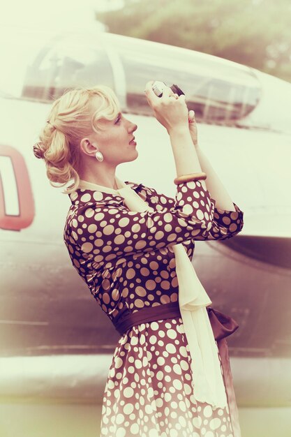 Vintage foto estilizada de hermosa chica con cámara de fotos y avión en el fondo