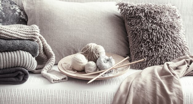 Vintage Holzstricknadeln und -fäden zum Stricken auf einem gemütlichen Sofa mit Kissen und Pullovern