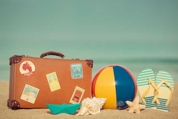 Vintage Koffer und Flipflops am Sandstrand gegen blaues Meer und Himmel