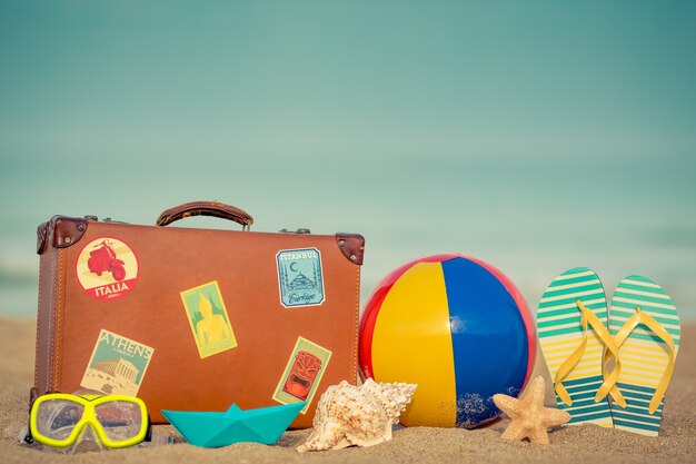 Vintage Koffer und Flipflops am Sandstrand gegen blaues Meer und Himmel