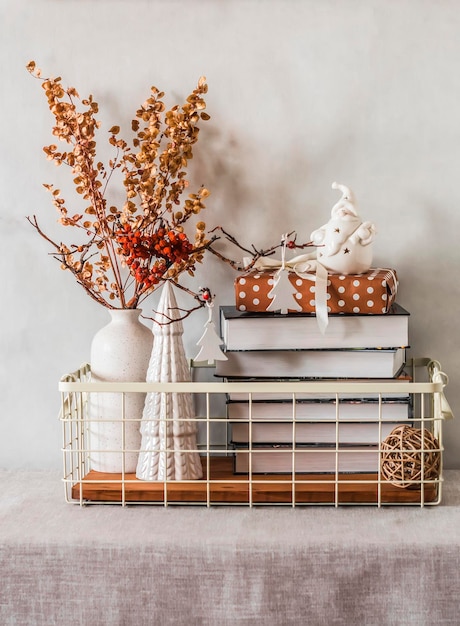 Vintage-Korb aus Metall mit Büchern, getrockneten Blumen, Keramik, Weihnachtsschmuck, Geschenkbox auf dem Tisch in einem gemütlichen Interieur