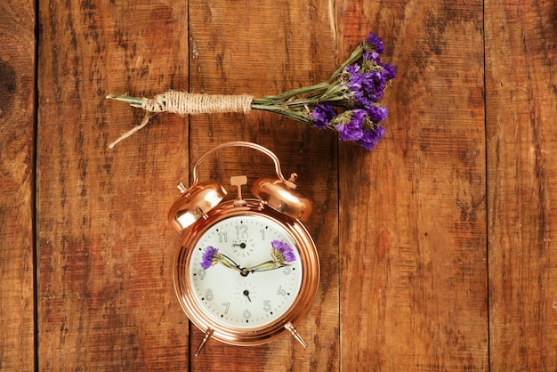 Vintage lindo despertador feito de metal dourado com flores azuis em vez de ponteiros de relógios e pequeno buquê de flores na superfície de madeira Despertar Primavera Tempo para a primavera Foto conceitual