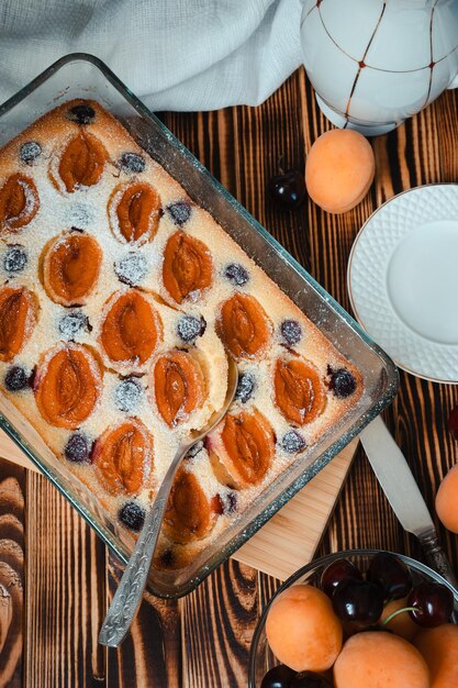 Vintage-Löffel in Aprikosenquarkkuchen mit Puderzucker und saisonalen Beeren auf Holztisch