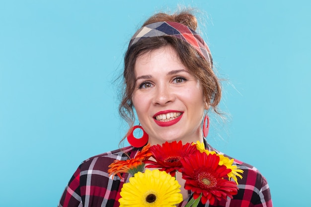 Vintage, moda y concepto florístico - mujer con gerberas divirtiéndose en estilo retro en la pared azul con espacio de copia.