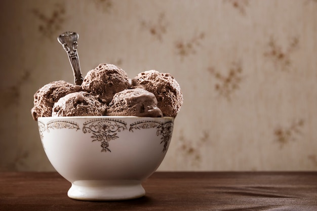 Vintage Schüssel und Löffel mit vielen Schokoladeneiskugeln. Köstliches hausgemachtes Eisdessert auf einem rustikalen Holztisch mit Vintage-Hintergrund.