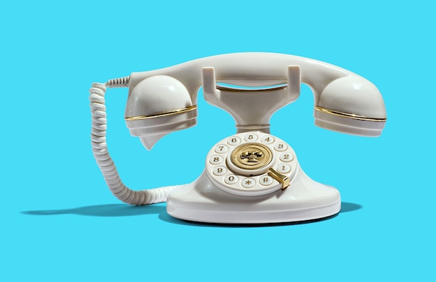 Vintage teléfono blanco con adornos dorados brillantes en el auricular y el dial colocado sobre fondo cian
