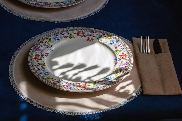 Vintage Tischdekoration Ein Schatten von einem Vorhang mit Quasten fällt auf einen Teller auf einer dunklen Samttischdecke