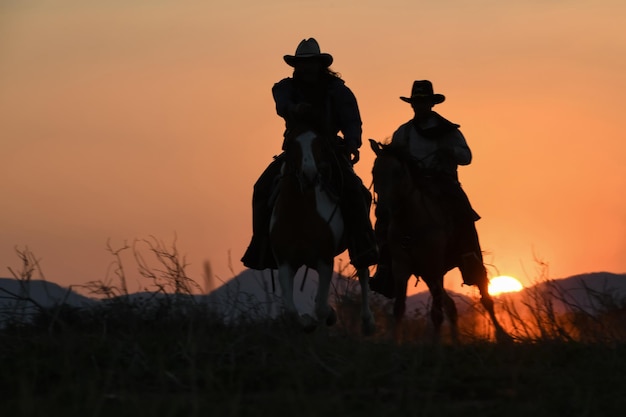 Vintage und Schatten einer Gruppe von Cowboys, die bei Sonnenuntergang zu Pferd galoppieren