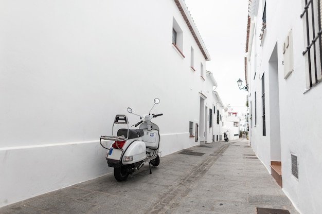 Vintage weißer roller steht auf einer straße nahe einer wand. schöne schmale straße mit weißen alten gebäuden in spanien.