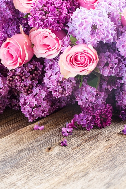 Violette Fliederblumen mit rosa Rosen auf Holztisch