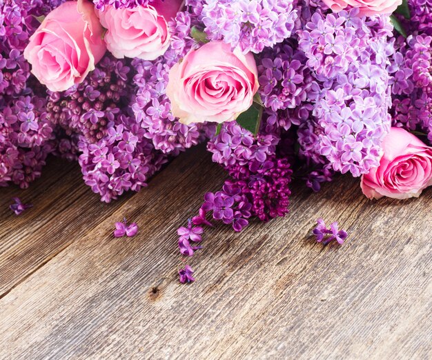 Violette Fliederblumen mit rosa Rosen auf Holztisch