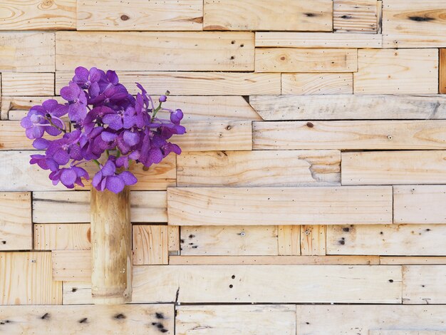 Violette wanda-orchidee im bambusvase, der an der hölzernen plankenwand hängt.