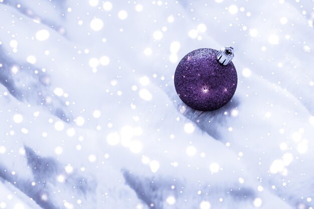 Violette Weihnachtskugeln auf flauschigem Fell mit schneeglitzerndem Luxus-Winterurlaub-Designhintergrund