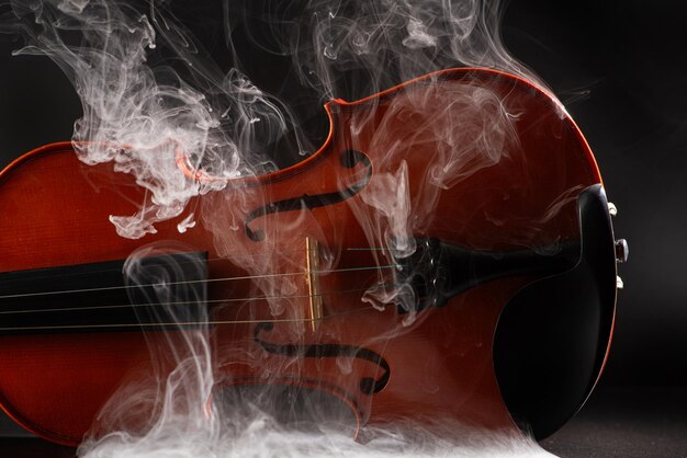 Violín y humo maravillosos detalles de un hermoso violín con humo en el entorno fondo oscuro enfoque selectivo