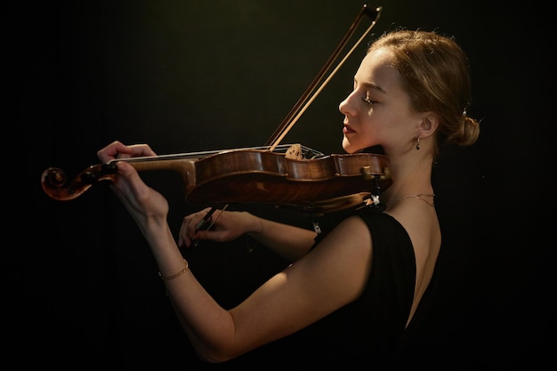 violinista feminina tocando música clássica dramaticamente sob a luz superior