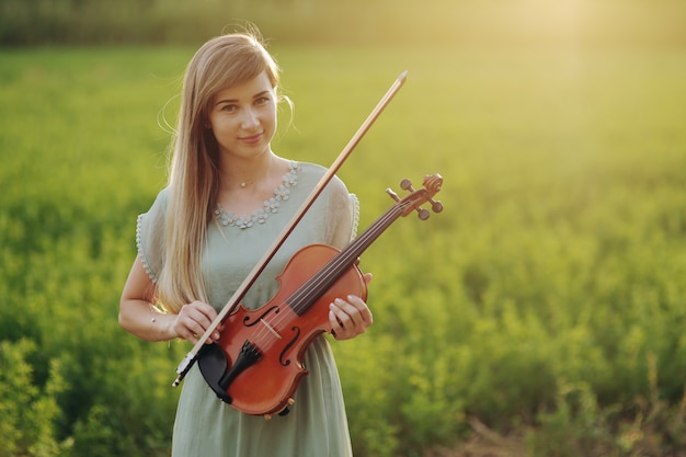 Violinista músico femenino sosteniendo el violín en sus manos en la luz del atardecer