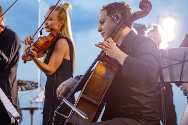 Violonchelista masculino tocando en orquesta en concierto al aire libre