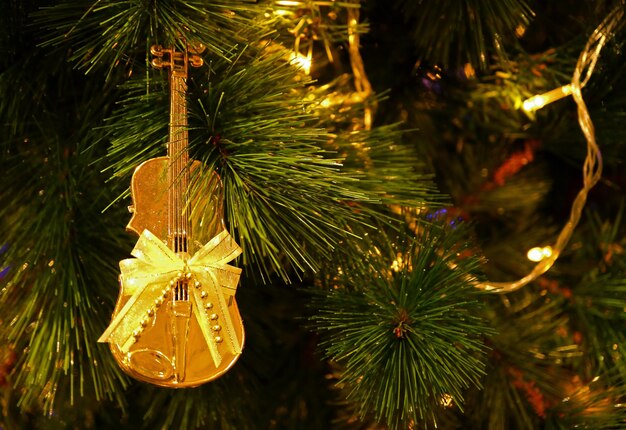 Violonchelo dorado brillante en forma de lazo con cinta Adorno navideño colgado en el árbol de Navidad