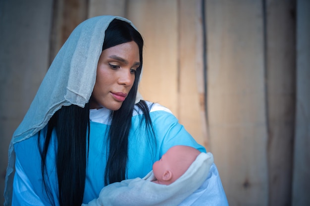 Virgen maría transexual sosteniendo y mirando al niño Jesús con ternura en un Belén