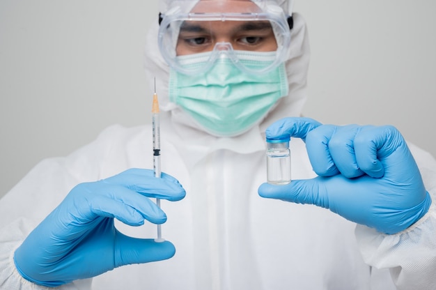 Virologista com traje de proteção individual segurando seringa e frasco de vacina