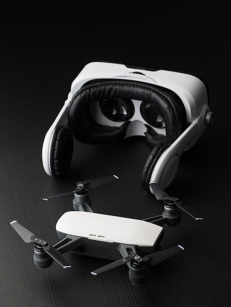 Foto virtual-reality-brille und drohne. draufsicht über quadcopter und vr kopfhörer auf dunklem holztisch.