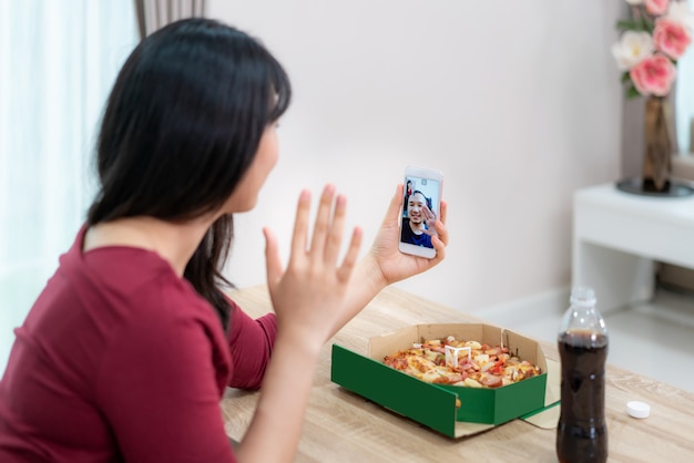 Virtuelle Happy Hour der asiatischen Frau, die Abendessen trifft und Pizza zusammen mit ihrem Freund in der Videokonferenz mit digitalem Tablet online isst