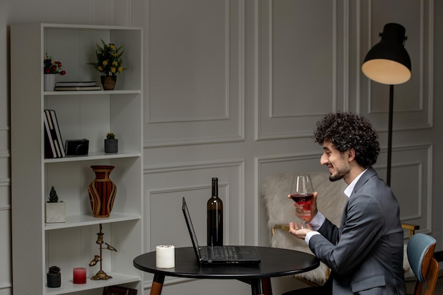 Virtuelle Liebe, hübscher, süßer Kerl im Anzug mit Wein auf einem Ferncomputer-Date mit Weinglas