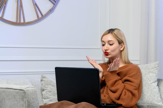 Foto virtuelle liebe süßes junges blondes mädchen im kuscheligen pullover am computer-distance-date, das küsse sendet