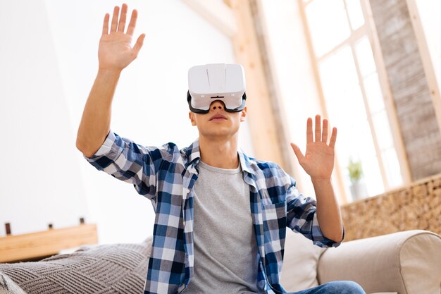 Virtuelle Realität. Konzentrierter, gut gebauter, stilvoller Jugendlicher, der ein VR-Headset trägt und sich auf dem Sofa entspannt