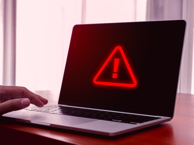 Virus-Alert Rotes Dreieck System gehackt Fehlerzeichen Malware Aufmerksamkeit Gefahr Symbol Systemfehler Warnung zeigt auf dem Bildschirm Anzeige von Laptop-Computer auf dem Tisch mit Geschäftsmann Hand roter Ton
