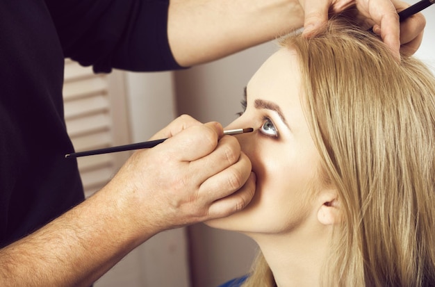 Visagiste aplicando maquiagem no rosto da menina com pincel na mão adorável mulher com pele saudável e m