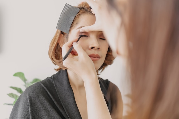 Visagistin trägt Make-up auf die Augen der Kunden auf