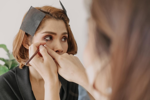 Visagistin trägt Make-up auf die Augen der Kunden auf