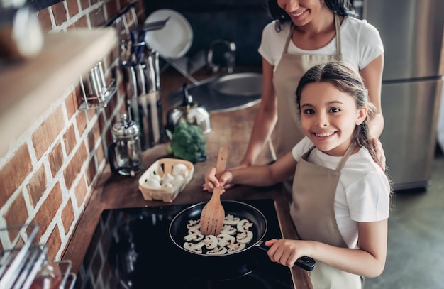 Visão aérea da filha e mãe fritando cogumelos no fogão juntos para jantar na cozinha e olhando para a câmera