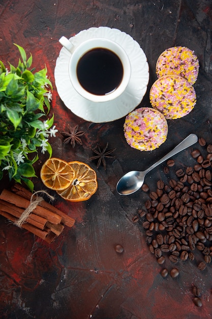 Visão aérea de deliciosos biscoitos de açúcar e uma xícara de café em um vaso de flores limões secos e grãos de fatias de canela em um fundo de cores misturadas.