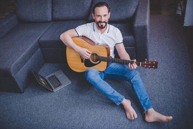 Visão aérea do homem tocando violão sentado no chão em casa