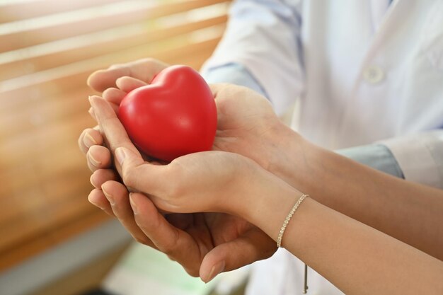 Visão aproximada das mãos do médico e do paciente segurando um coração vermelho Doação de órgãos de saúde e conceito de cardiologia