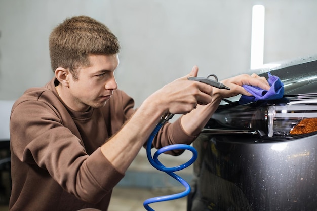 Visão aproximada de um jovem trabalhador caucasiano limpando os faróis do carro com um pano de microfibra azul