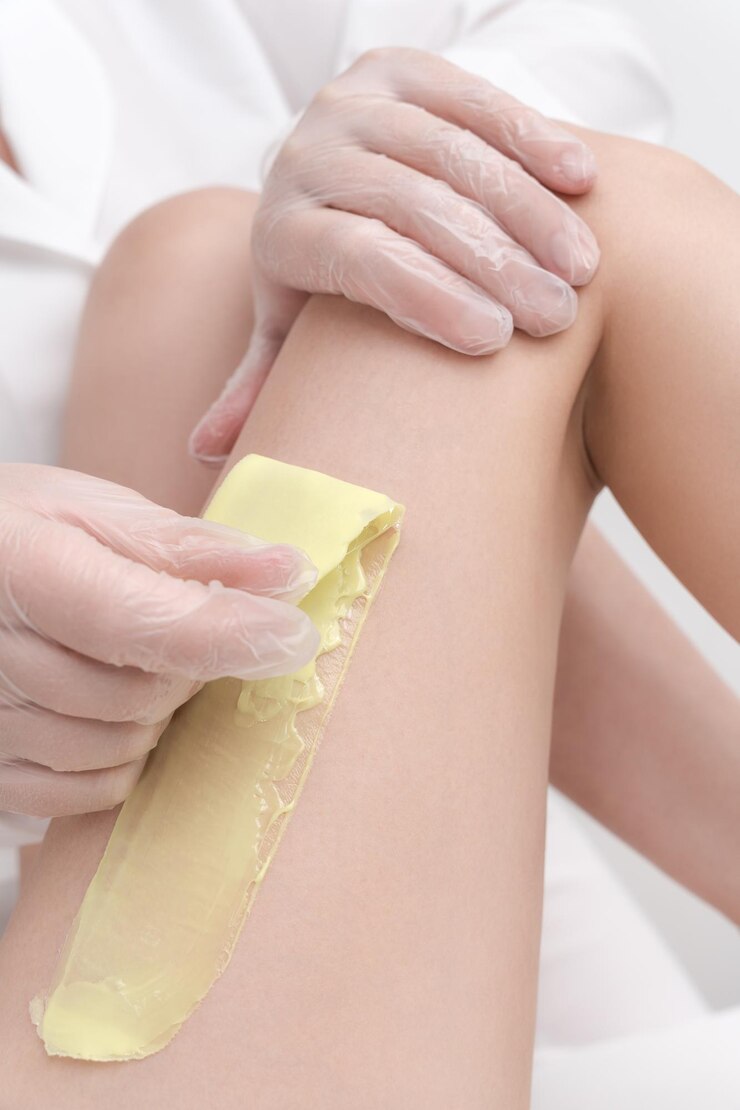 Visão aproximada do cosmetologista removendo pêlos na perna feminina usando cera quente em salão de beleza profissional