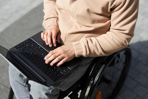 Visão de alto ângulo de um jovem com deficiência digitando no laptop que trabalha online ao ar livre