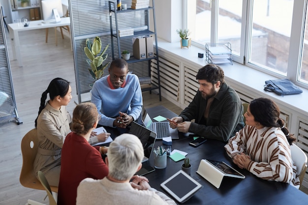 Visão de alto ângulo em um grupo diversificado de executivos à mesa durante uma reunião de briefing no escritório, foco no sorridente homem afro-americano