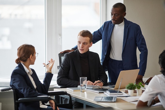 Visão de corpo inteiro em diversos grupos de empresários na mesa de reunião no escritório com mulher usando cadeira de rodas em primeiro plano