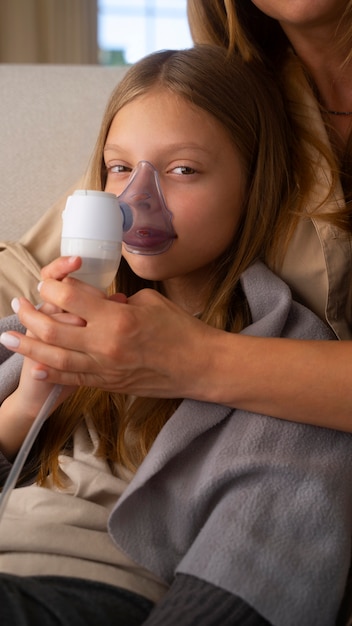Foto visão de mãe e filha usando nebulizador em casa para problemas de saúde respiratória