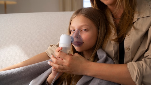 Foto visão de mãe e filha usando nebulizador em casa para problemas de saúde respiratória