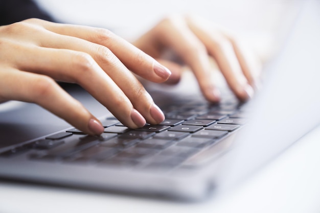 Visão detalhada das mãos de uma mulher digitando em um elegante ambiente de escritório de teclado de laptop suavemente desfocado no pano de fundo