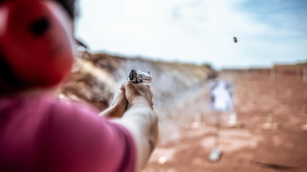 Visão detalhada do atirador segurando a arma e treinando tiro tático, foco na pistola. Campo de tiro.