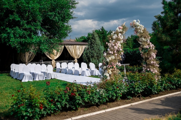 Foto visão geral da decoração da cerimônia de casamento no jardim no ar. decoração de casamento um arco feito de flores frescas, cadeiras cobertas para convidados