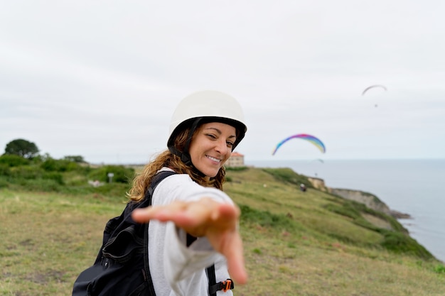 Visão horizontal de mulher com equipamento de parapente, alcançando a mão para a câmera. vista panorâmica de mulher aventureira praticando esportes de risco. estilo de vida de aventura e esporte.