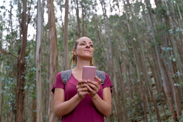 Visão horizontal de mulher usando smartphone no meio da floresta. conceito de destino de tecnologia, pessoas e viagens.